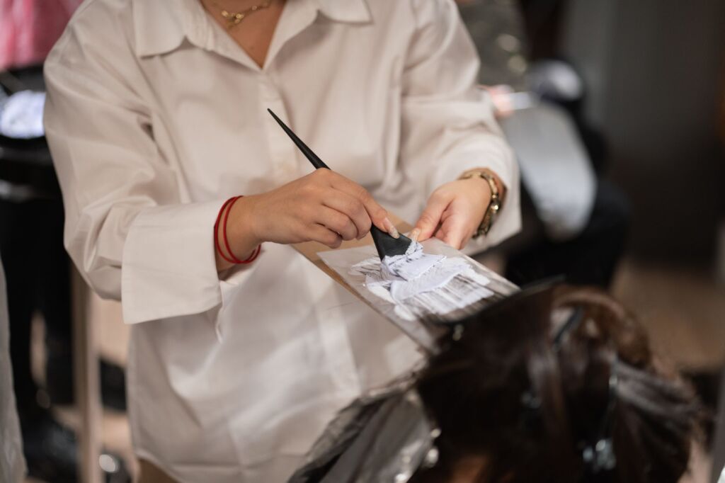 Friseurin trägt Haarbehandlung mit Pinsel auf Haarsträhnen auf im Salon