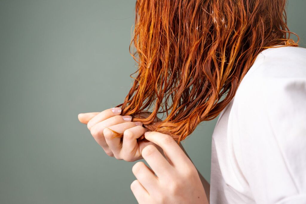 Frau hält nasse rote Haarsträhne zwischen den Händen zum Stretch-Test