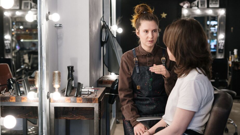Hairstylist consults with client seated in salon chair during hair analysis appointment