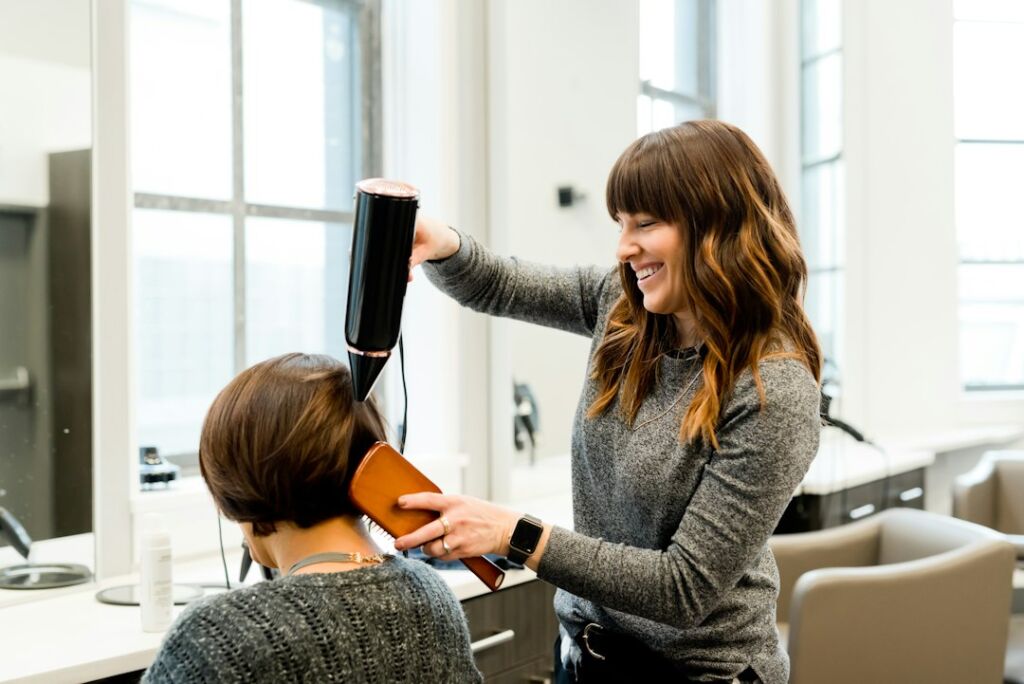 Freundliche Stylistin im modernen Salon beim Styling einer Kundin, helles offenes Ambiente