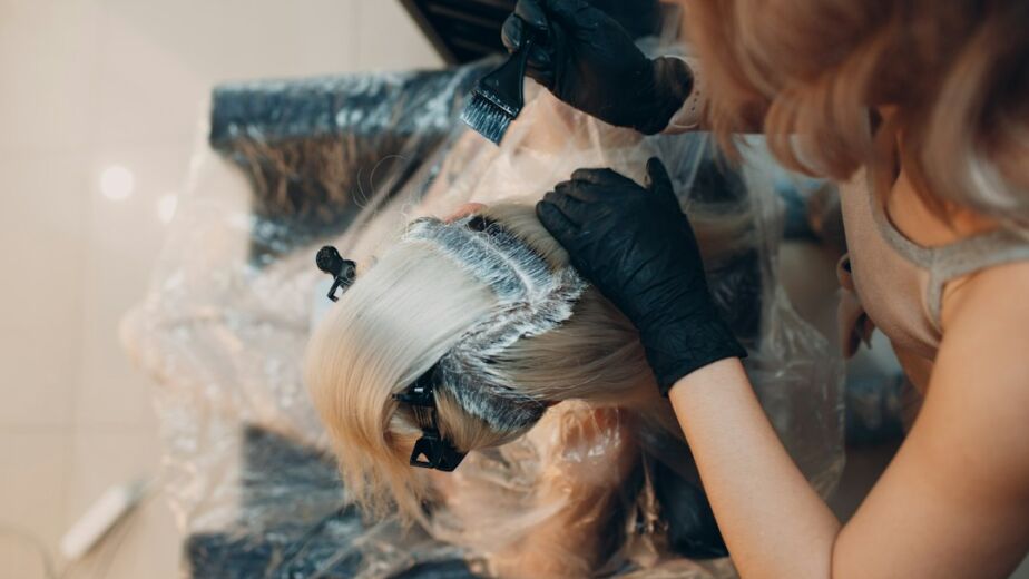 Professionelle Haarcoloristin beim Auftragen von Balayage-Farbe auf blondes Haar im Salon