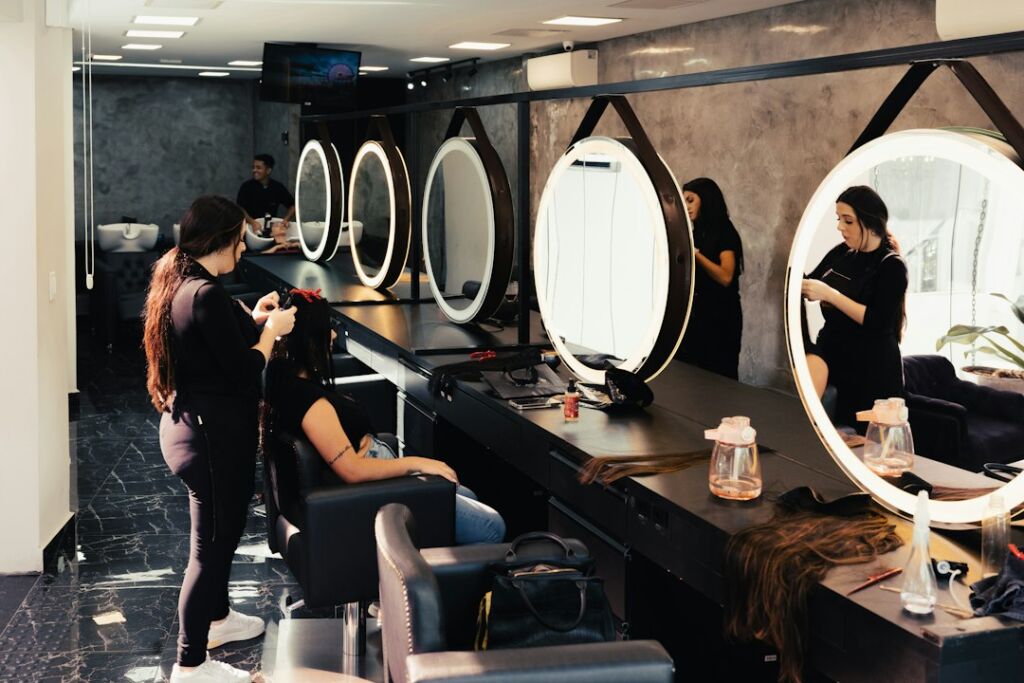Friseurin arbeitet mit Kundin im Salon vor beleuchteten runden Spiegeln