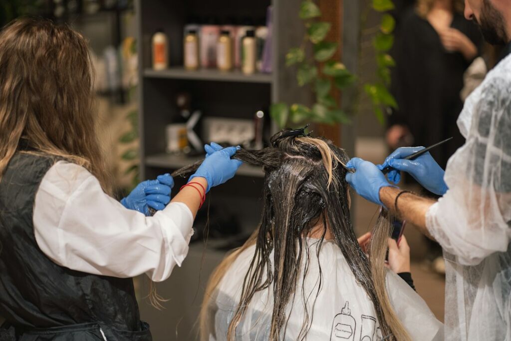 Zwei Friseurinnen tragen Haarfarbe auf dunkles Haar einer Kundin auf, Balayage-Sitzung im Salon