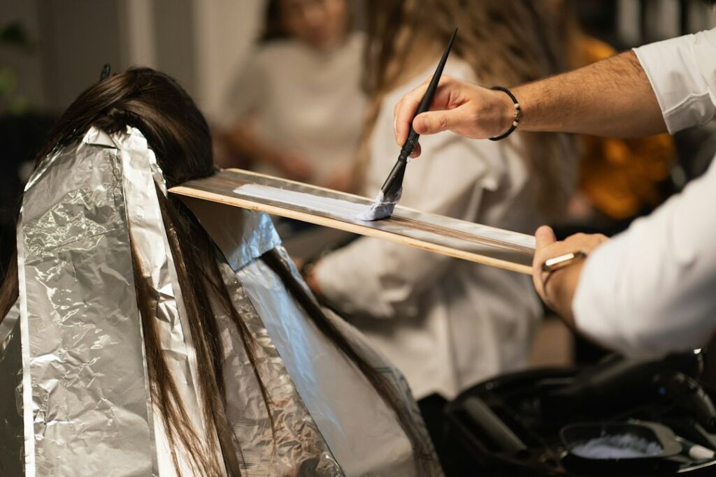 Coiffeur malt Balayage-Farbe freihand mit einem Pinsel auf dunkles Haar