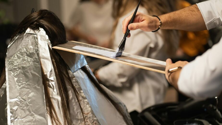 Stylist applying balayage color to dark hair with a brush on a palette