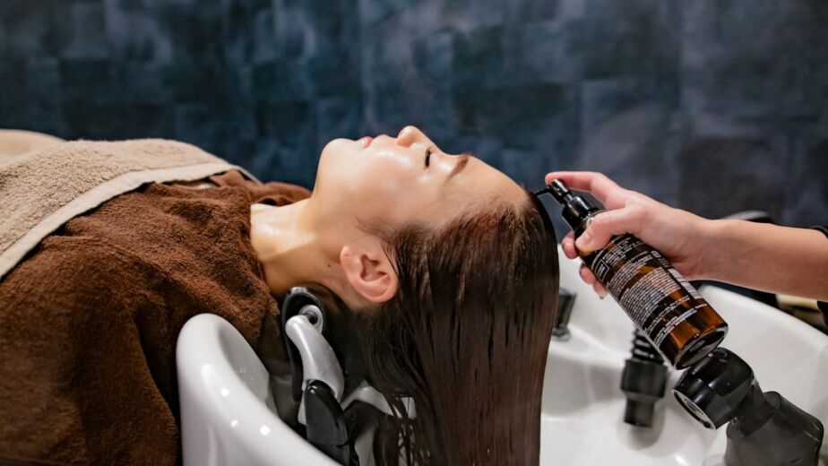 Frau beim Haar-Gloss-Treatment im Salon, Pflegeprodukt wird am Waschbecken aufgetragen